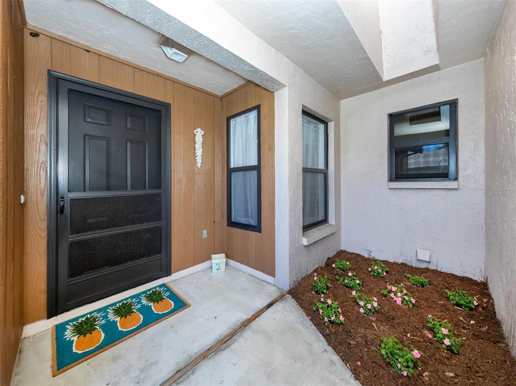 A covered entryway features a dark storm door, wood-paneled walls, and a small garden bed — 401 CURRY STREET UNIT 66, NOKOMIS, FL