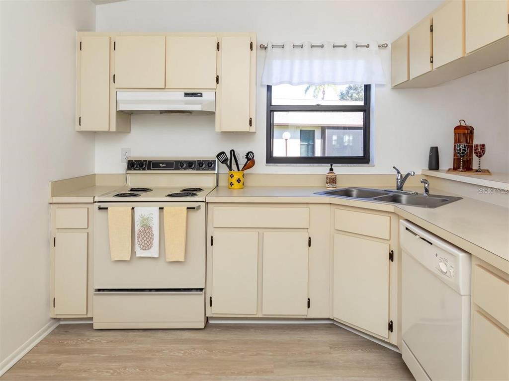 A kitchen with cream-colored cabinets, white appliances, a double sink, and light wood-look flooring — 401 CURRY STREET UNIT 66, NOKOMIS, FL