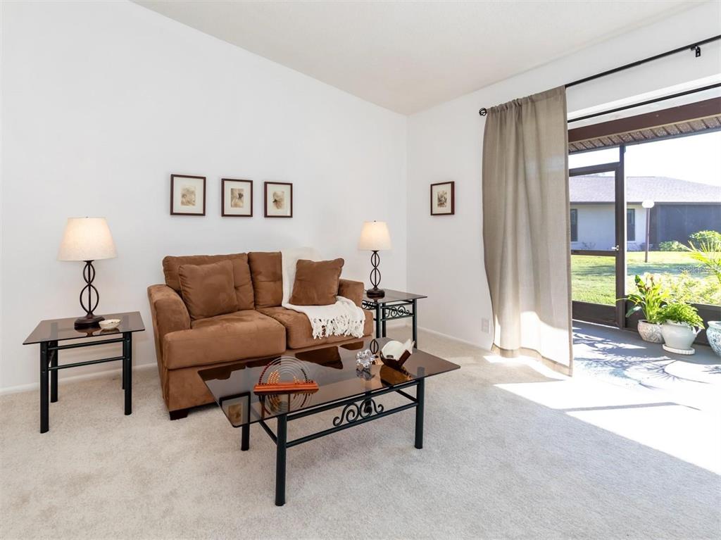 A living room features a brown sofa, glass-topped tables, and a sliding door to a patio — 401 CURRY STREET UNIT 66, NOKOMIS, FL