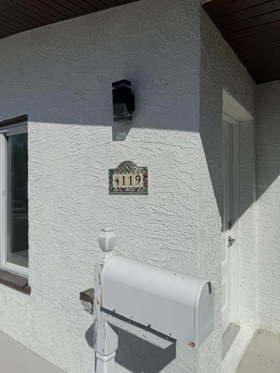 A white mailbox stands in front of a textured white wall with a house number plaque — 4119 HARRISBURG STREET NE, ST PETERSBURG, FL