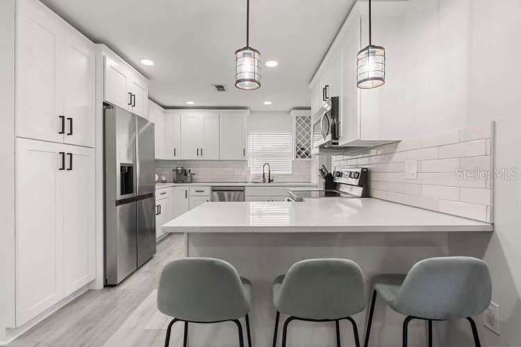 A modern white kitchen features stainless steel appliances, a quartz peninsula, and three gray stools — 13 FANFAIR, ORLANDO, FL