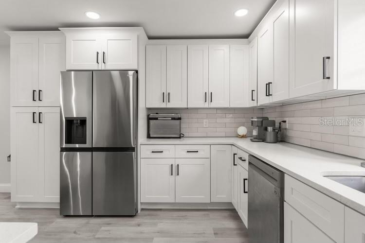 A modern kitchen features white shaker cabinets, stainless steel appliances, and a light subway tile backsplash — 13 FANFAIR, ORLANDO, FL
