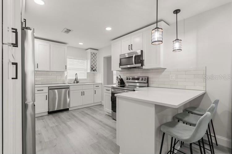 A modern kitchen features white cabinets, stainless steel appliances, a breakfast bar, and light flooring — 13 FANFAIR, ORLANDO, FL