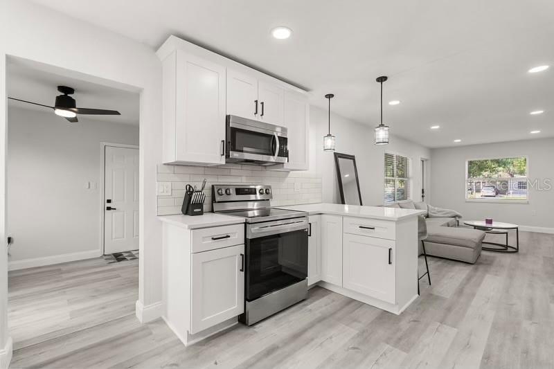 A kitchen with white cabinets, stainless steel appliances, and light wood flooring opens to a living area — 13 FANFAIR, ORLANDO, FL