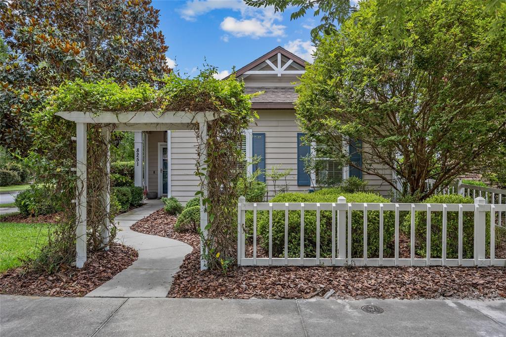 A white wooden arbor stands over a concrete walkway leading to a tan house — 8251 SW 78TH LANE, GAINESVILLE, FL