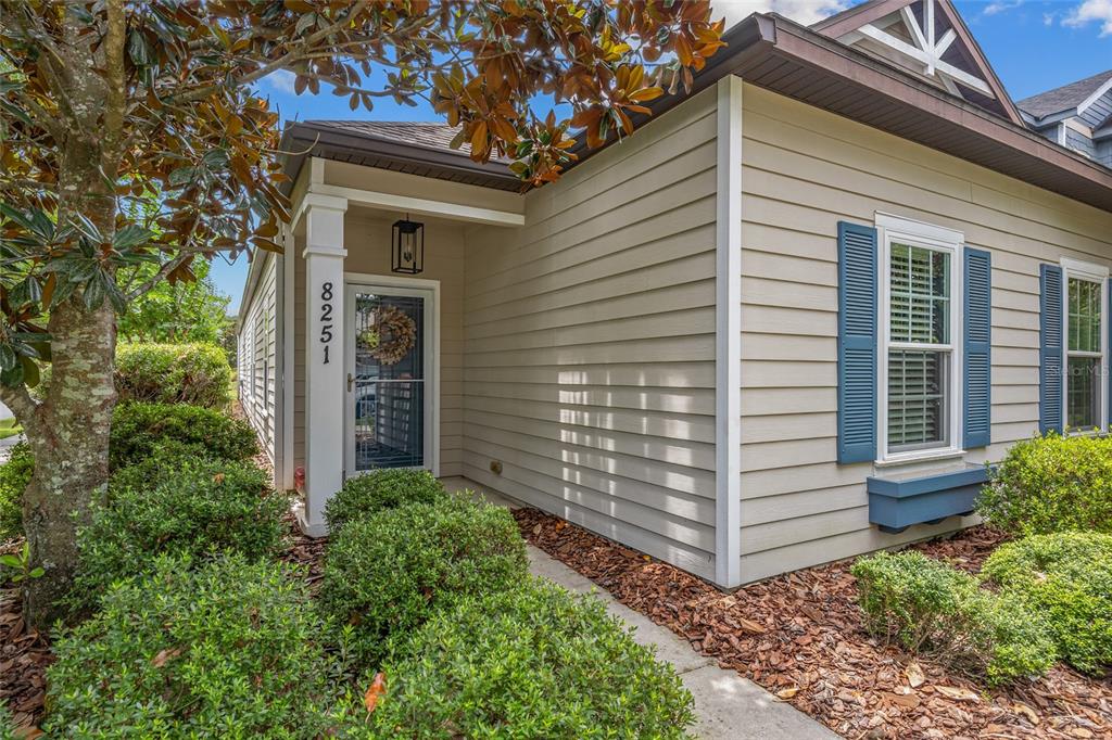 The exterior of a tan house features a covered entryway, blue shutters, and landscaping — 8251 SW 78TH LANE, GAINESVILLE, FL