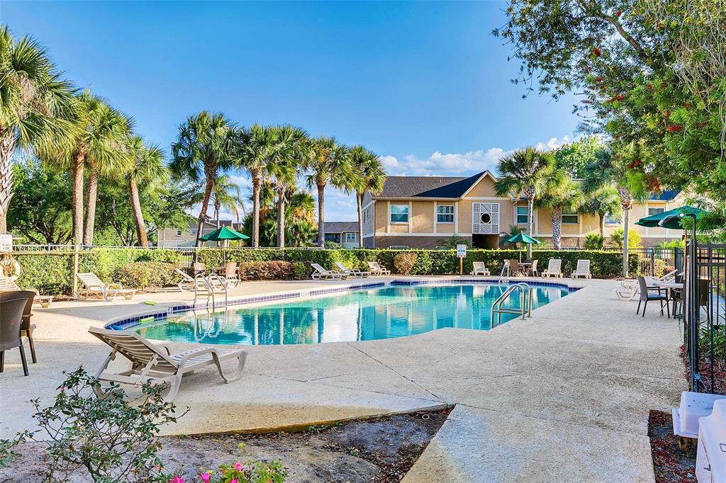A swimming pool surrounded by lounge chairs, palm trees, and a multi-story apartment building — 2401 BARLEY CLUB COURT UNIT 2, ORLANDO, FL