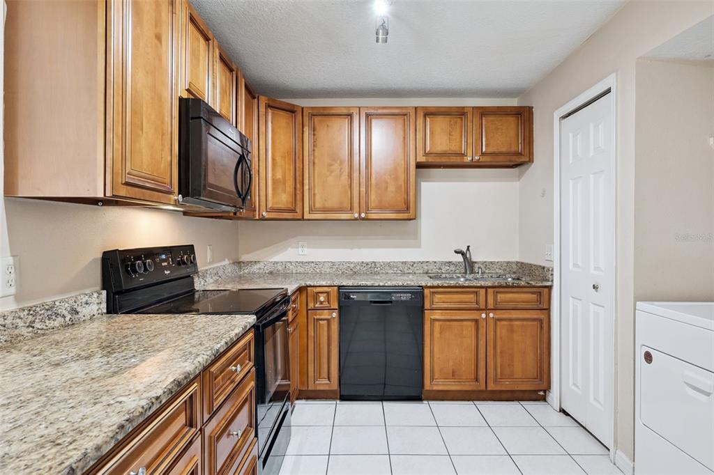 A kitchen features wood cabinets, granite countertops, black appliances, and white tile flooring — 2401 BARLEY CLUB COURT UNIT 2, ORLANDO, FL