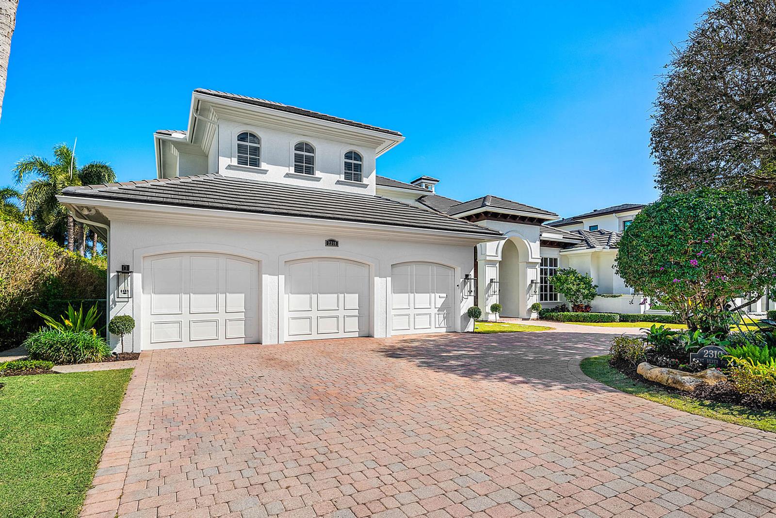 A three-car garage with white doors sits in front of a two-story white house — 2310 W Silver Palm Road, Boca Raton FL 33432, BOCA RATON, FL