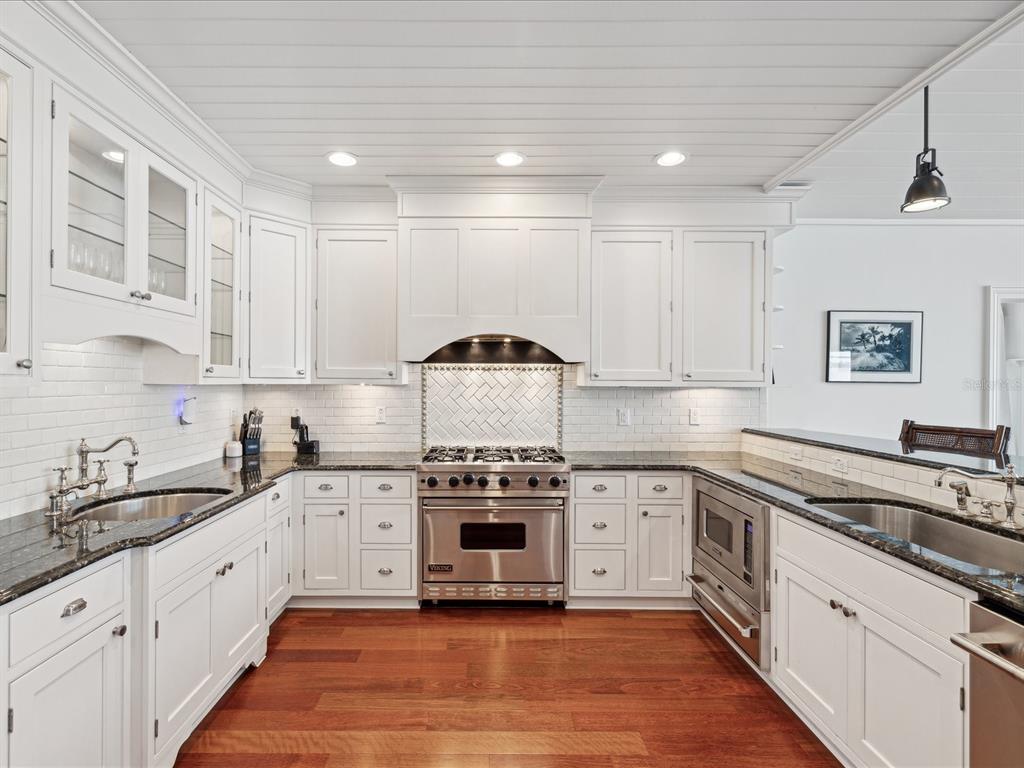 A white kitchen features dark granite countertops, stainless steel appliances, and hardwood flooring — 450 22ND STREET, BELLEAIR BEACH, FL