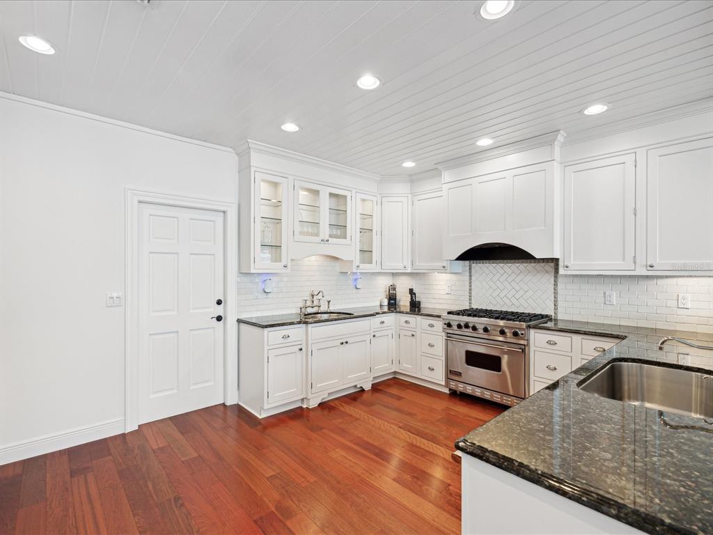 A white kitchen features dark granite countertops, stainless steel appliances, and hardwood flooring — 450 22ND STREET, BELLEAIR BEACH, FL