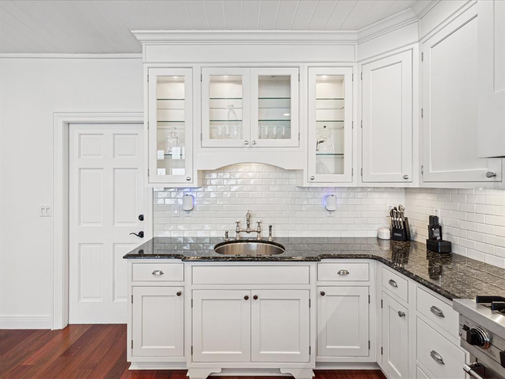 A kitchen features white cabinets, a dark granite countertop, a stainless steel sink, and backsplash — 450 22ND STREET, BELLEAIR BEACH, FL