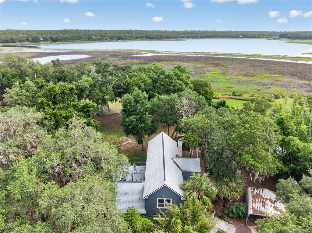 An aerial view shows a dark-sided house with a grey roof surrounded by trees near a lake — 104 LONG POND WAY, HAWTHORNE, FL