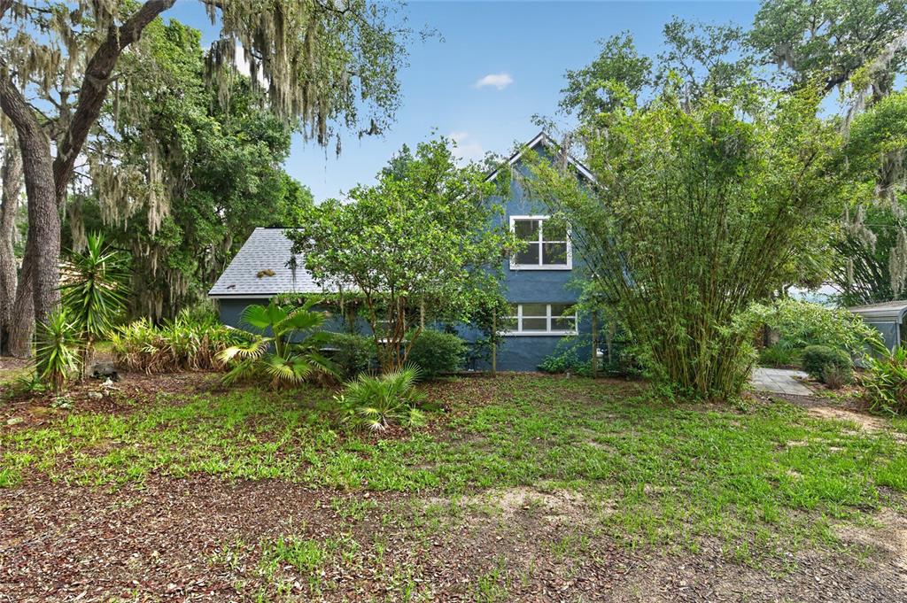 A blue two-story house sits in a wooded yard with palm trees and tall bamboo — 104 LONG POND WAY, HAWTHORNE, FL
