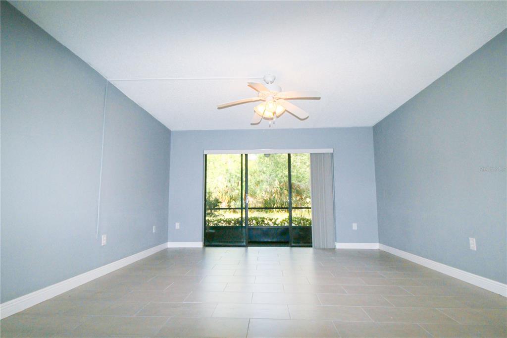 A living room with light blue walls, tile flooring, a ceiling fan, and sliding glass doors — 3232 LAKE PINE WAY E UNIT G1, TARPON SPRINGS, FL