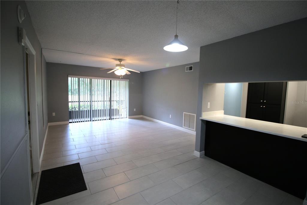An open-concept living area features light tile flooring, gray walls, and a kitchen pass-through window — 3232 LAKE PINE WAY E UNIT G1, TARPON SPRINGS, FL