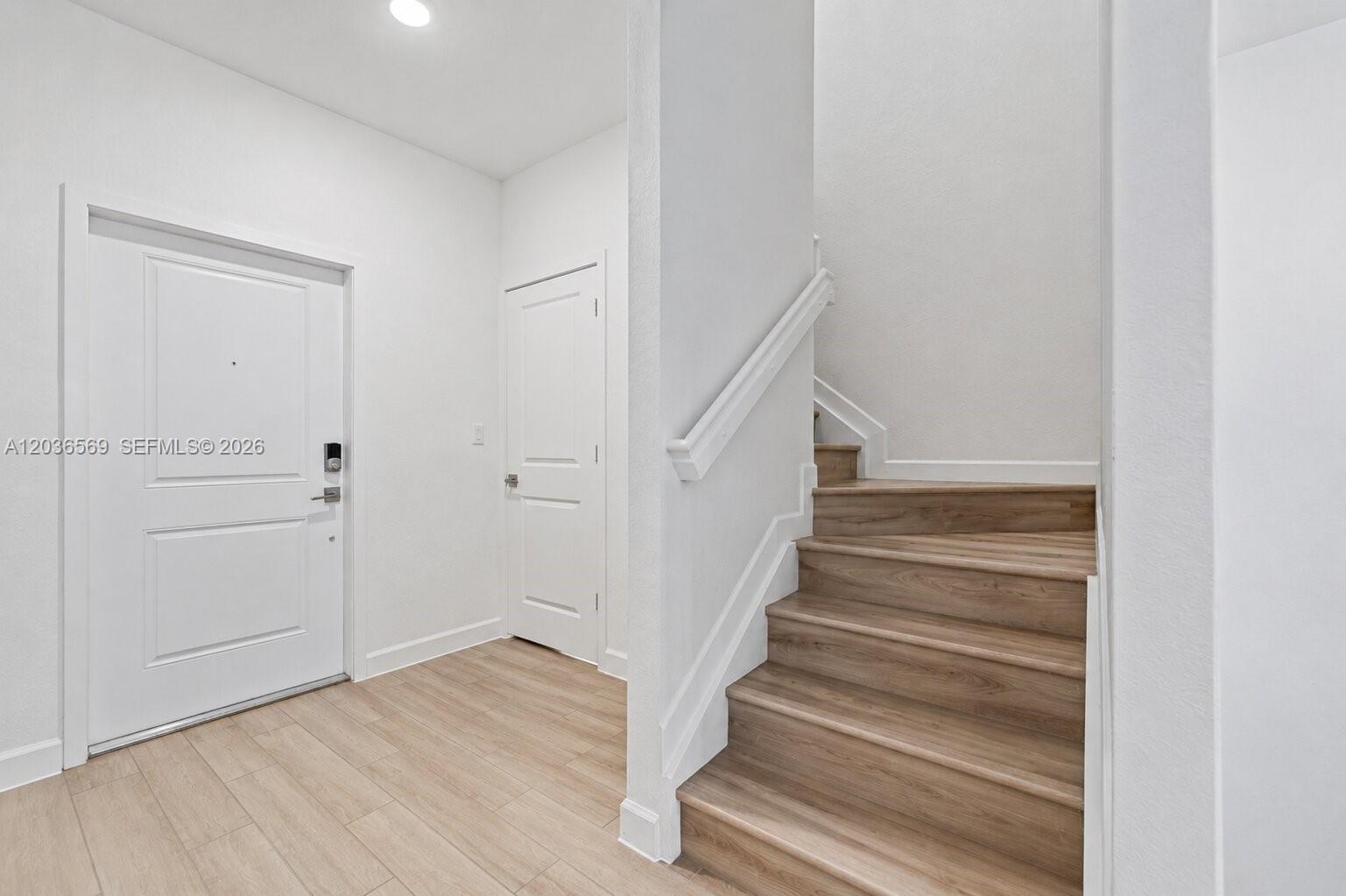 An entryway features light wood-look flooring, a white front door, and a wooden staircase — 2448 SE 10th Ct, Homestead FL 33035, HOMESTEAD, FL