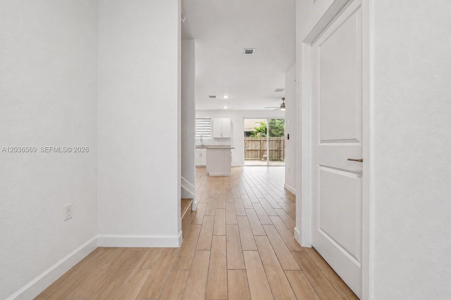 A hallway with wood-look tile flooring leads to an open kitchen and sliding glass doors — 2448 SE 10th Ct, Homestead FL 33035, HOMESTEAD, FL