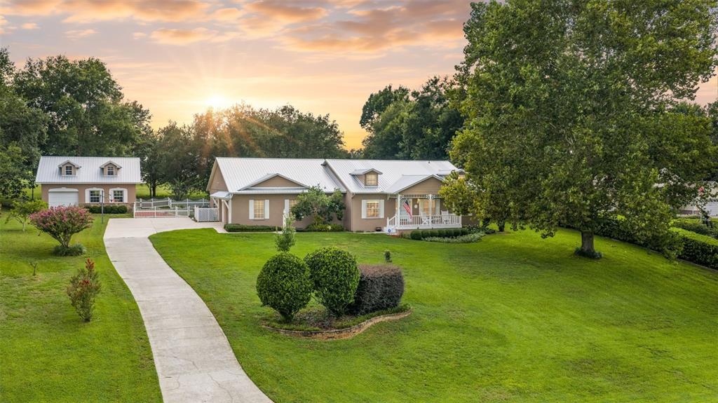 A single-story house with a metal roof and detached garage sits on a grassy lot — 12728 CYNTHIA LANE, CLERMONT, FL