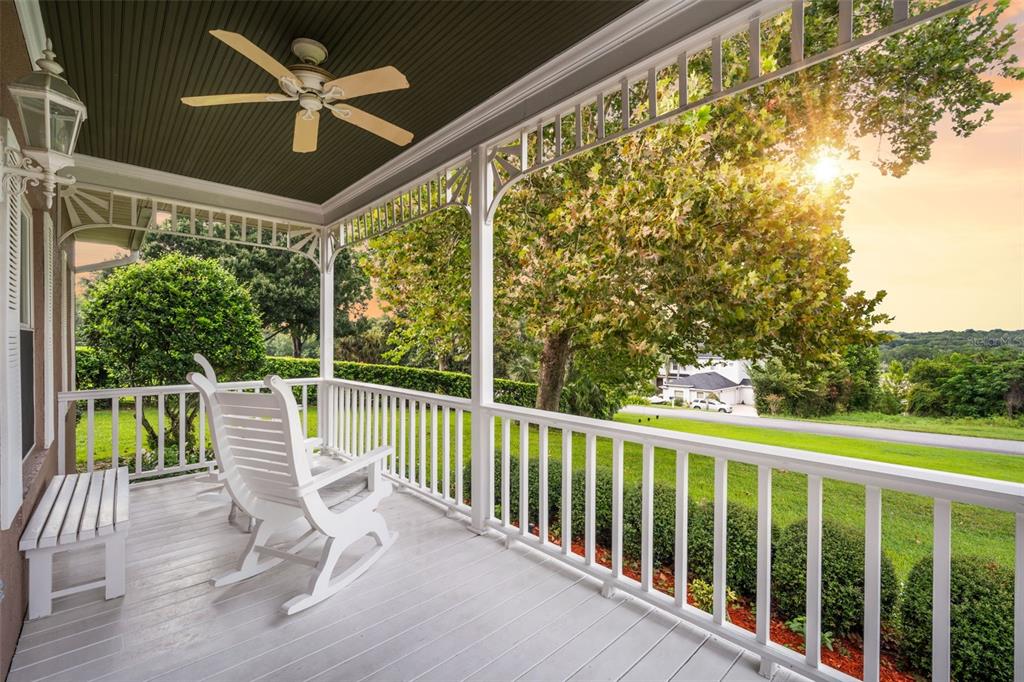 A covered porch features white railings, rocking chairs, a ceiling fan, and a sunset view — 12728 CYNTHIA LANE, CLERMONT, FL