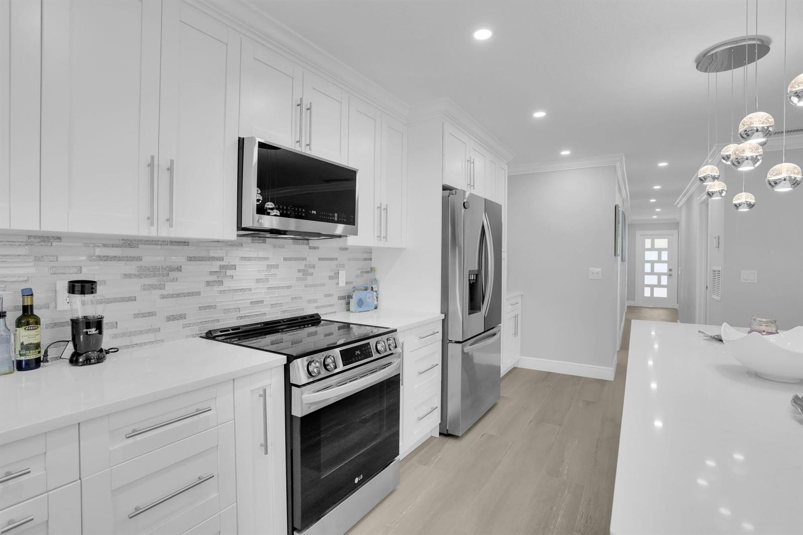 A modern white kitchen features stainless steel appliances, quartz countertops, and a glass pendant light fixture — 540 High Point Drive # A, Delray Beach FL 33445, DELRAY BEACH, FL
