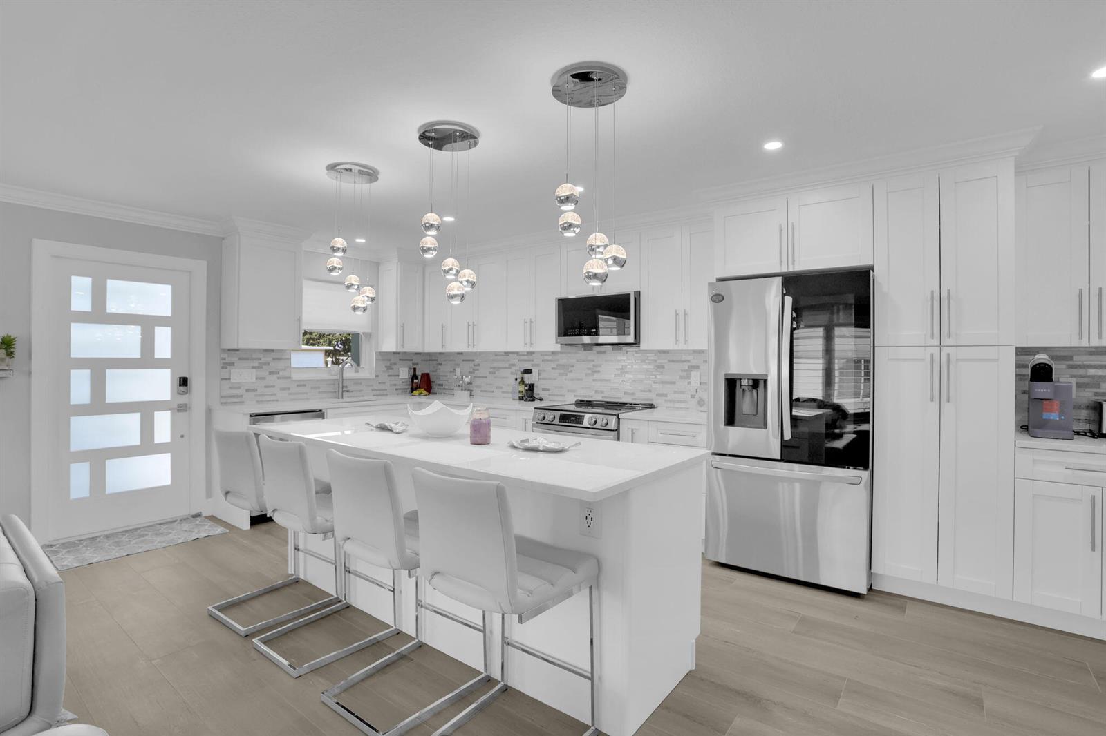 A modern white kitchen features a central island with bar seating and stainless steel appliances — 540 High Point Drive # A, Delray Beach FL 33445, DELRAY BEACH, FL