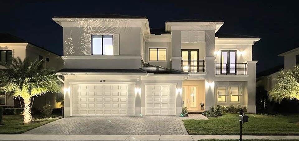 A two-story house with a paved driveway, two garage doors, and exterior lighting at night — 6930 NW 27th Avenue, Boca Raton FL 33496, BOCA RATON, FL