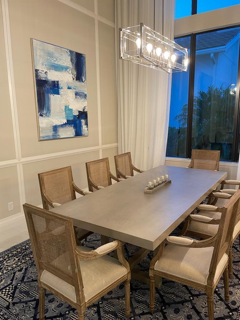 A dining room features a concrete table, cane-back chairs, a blue abstract painting, and chandelier — 6930 NW 27th Avenue, Boca Raton FL 33496, BOCA RATON, FL