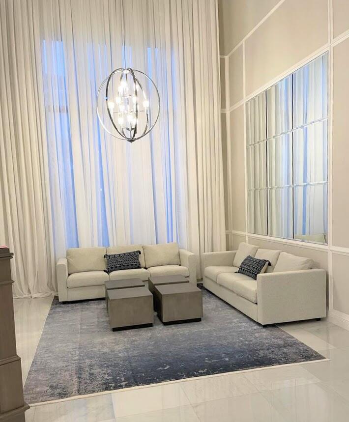 A living room features two beige sofas, square grey ottomans, a blue rug, and curtains — 6930 NW 27th Avenue, Boca Raton FL 33496, BOCA RATON, FL