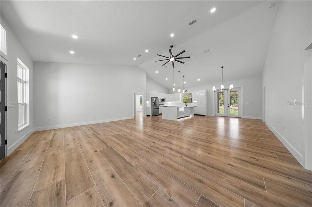 An open-concept living area features light wood-look flooring, white walls, and a modern kitchen — 4438 SW 179TH PLACE, OCALA, FL
