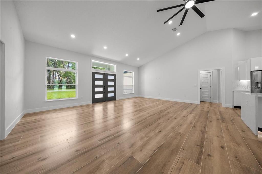 A spacious living room features light wood-look flooring, white walls, and a vaulted ceiling — 4438 SW 179TH PLACE, OCALA, FL