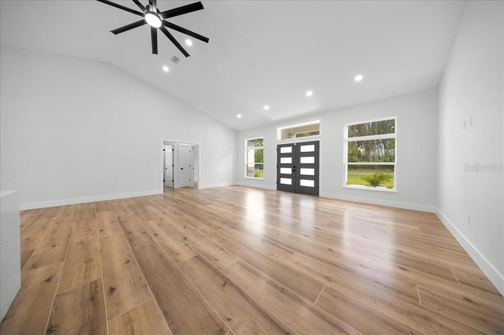 A spacious living room features light wood-look flooring, a vaulted ceiling, and a dark front door — 4438 SW 179TH PLACE, OCALA, FL