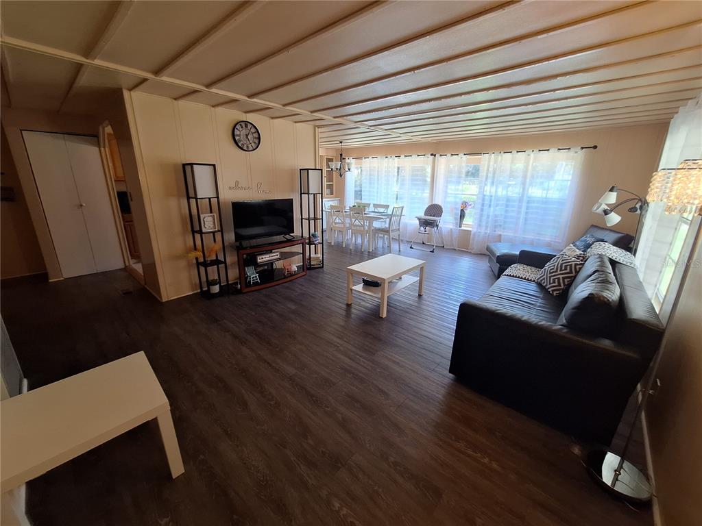 A living room with dark wood-look flooring, a black sofa, and an adjacent dining area — 3911 LOURY DRIVE, WESLEY CHAPEL, FL