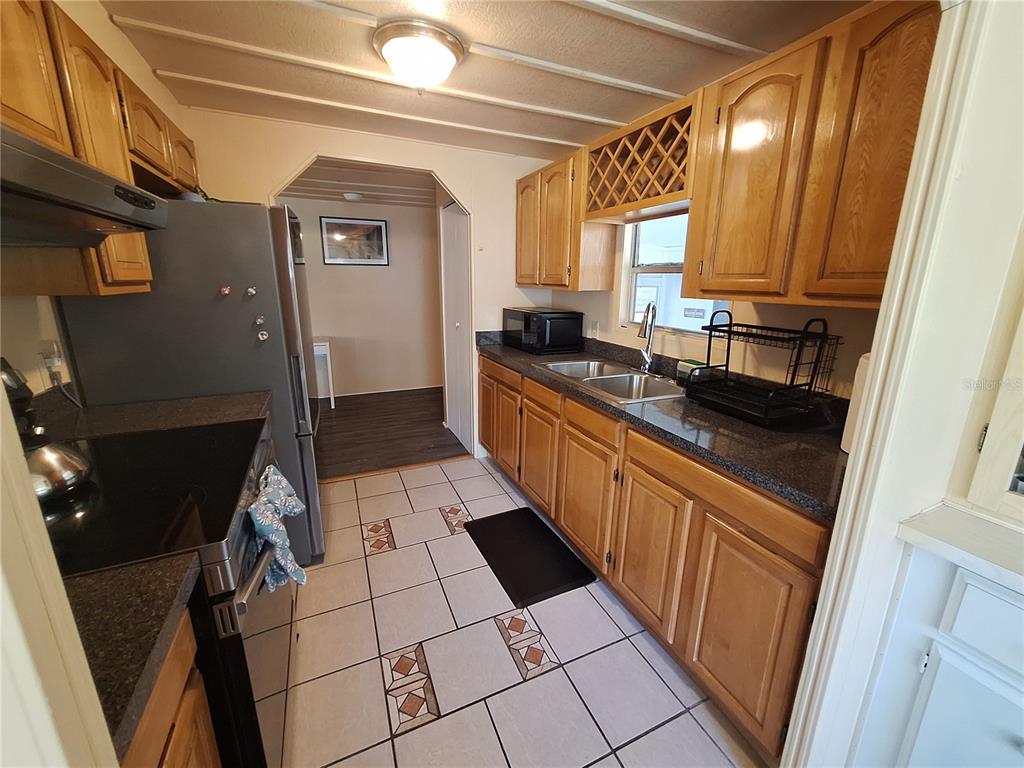 A kitchen features wood cabinets, dark countertops, tile flooring, and stainless steel appliances — 3911 LOURY DRIVE, WESLEY CHAPEL, FL
