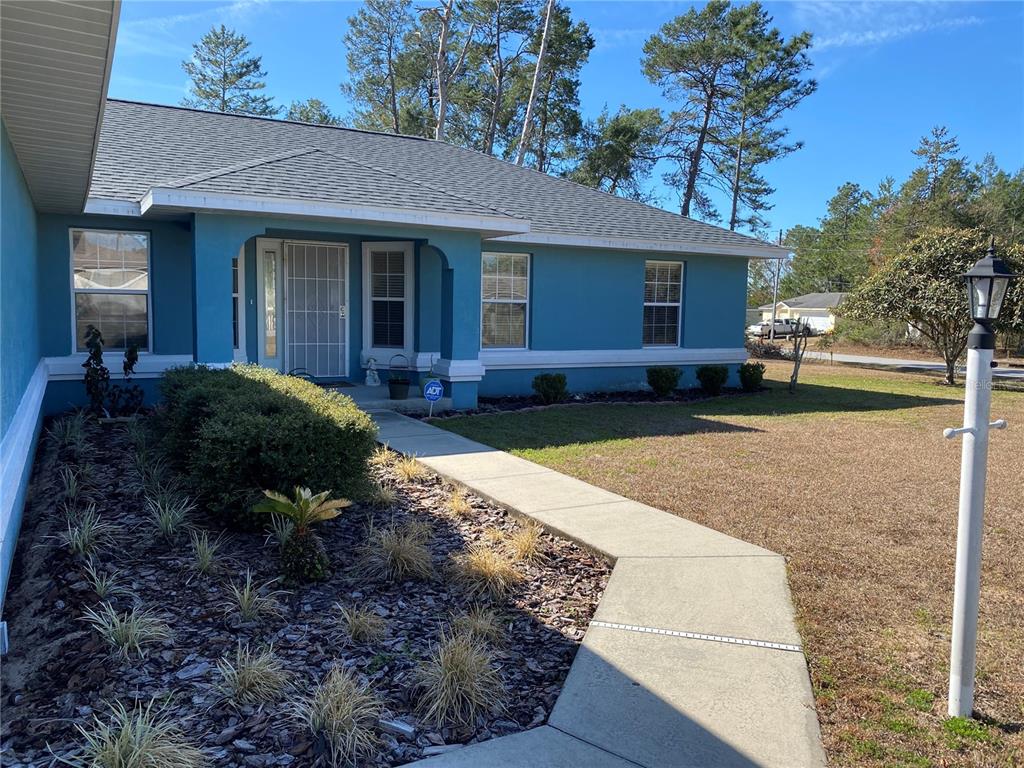 A blue single-story house features a concrete walkway leading to a covered front entrance — 3658 SW 127TH LANE ROAD, OCALA, FL