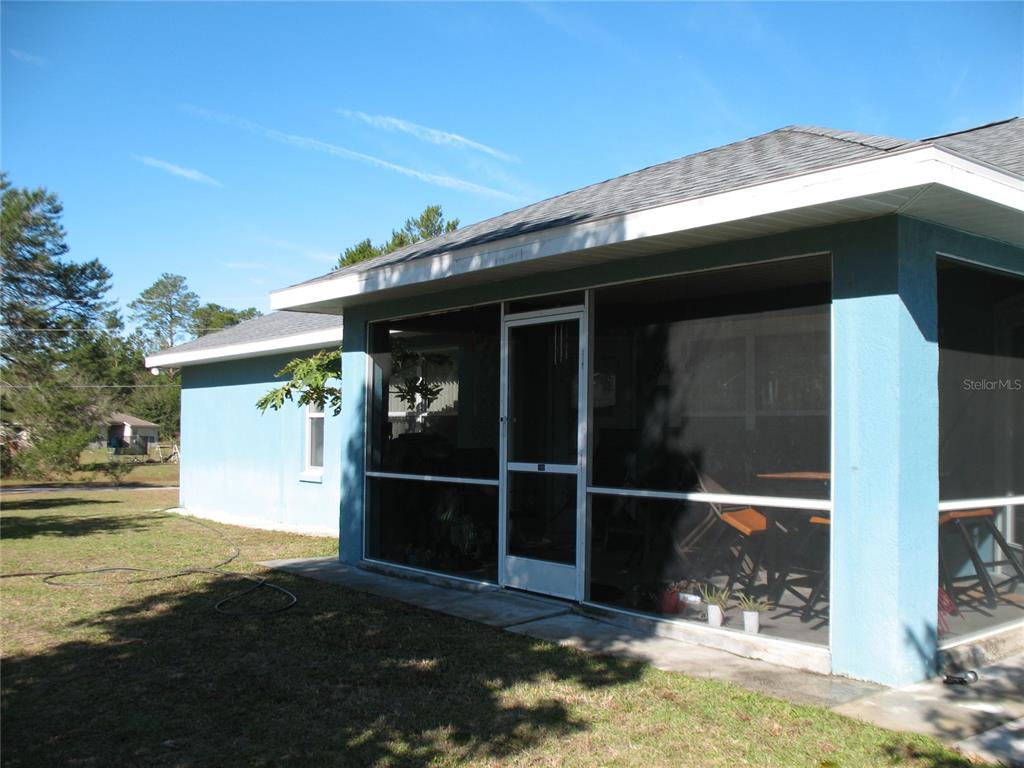 A blue house features a screened-in porch with a door and a concrete patio — 3658 SW 127TH LANE ROAD, OCALA, FL