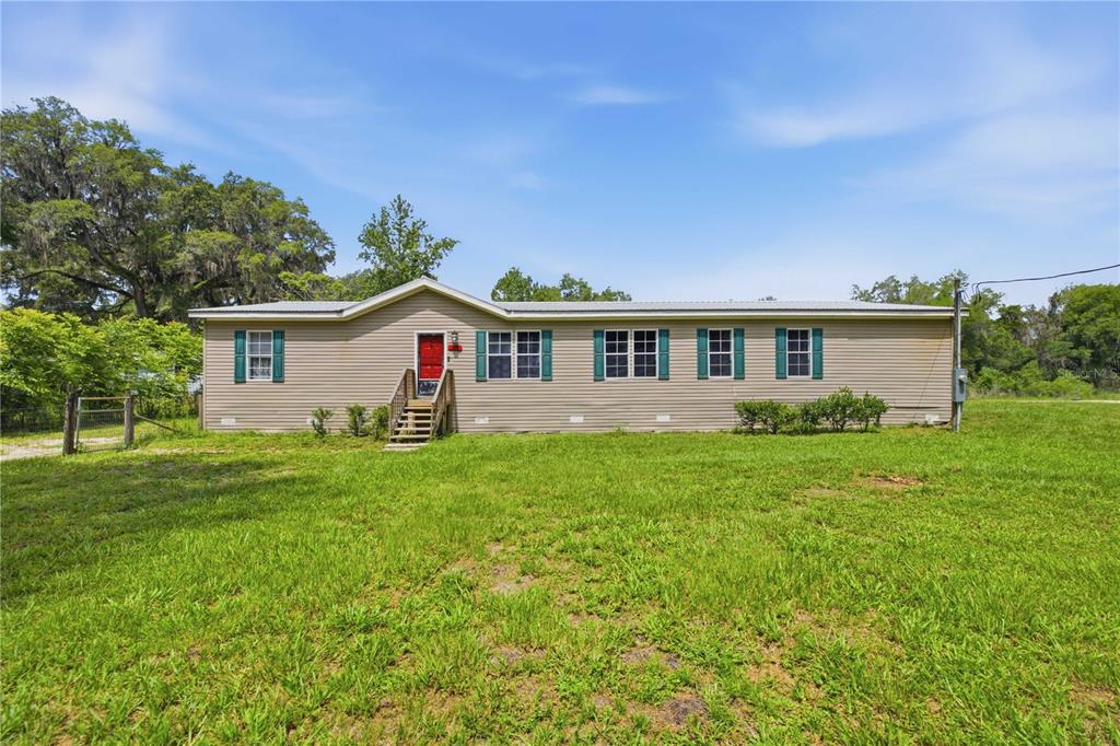 A single-story tan manufactured home with a red front door sits on a grassy lot — 16520 NE 42ND AVENUE, CITRA, FL