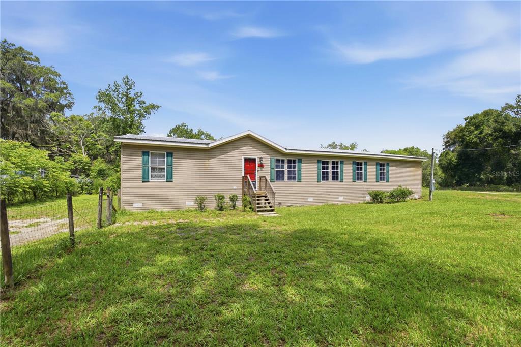 A tan single-story manufactured home with a red front door sits on a grassy lot — 16520 NE 42ND AVENUE, CITRA, FL