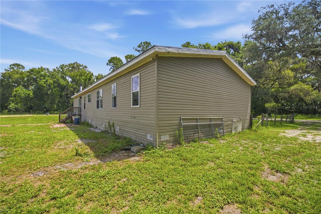 The exterior of a tan, single-story manufactured home sits on a grassy lot with trees — 16520 NE 42ND AVENUE, CITRA, FL