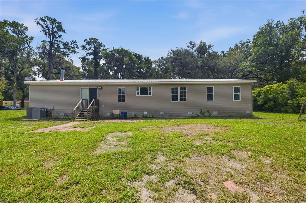 A single-story manufactured home with beige siding sits on a grassy lot with trees — 16520 NE 42ND AVENUE, CITRA, FL