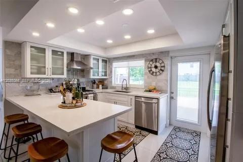 A modern kitchen features white cabinetry, a quartz island with bar stools, and stainless appliances — 933 NW 106th Ave Cir, Miami FL 33172, MIAMI, FL