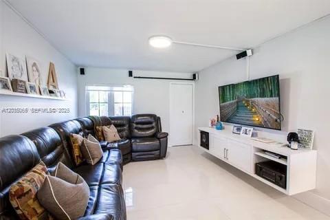 A living room features a dark leather sectional sofa, a wall-mounted television, and white cabinetry — 933 NW 106th Ave Cir, Miami FL 33172, MIAMI, FL
