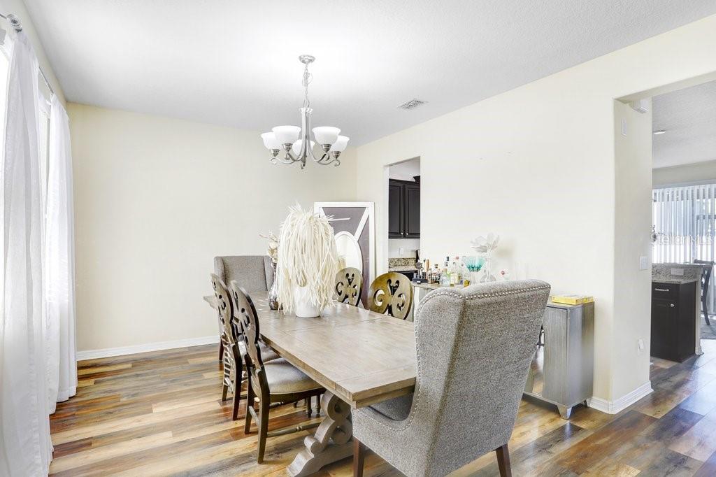A dining room features a wooden table, upholstered chairs, a chandelier, and wood-look flooring — 13117 ROYAL PINES AVENUE, RIVERVIEW, FL