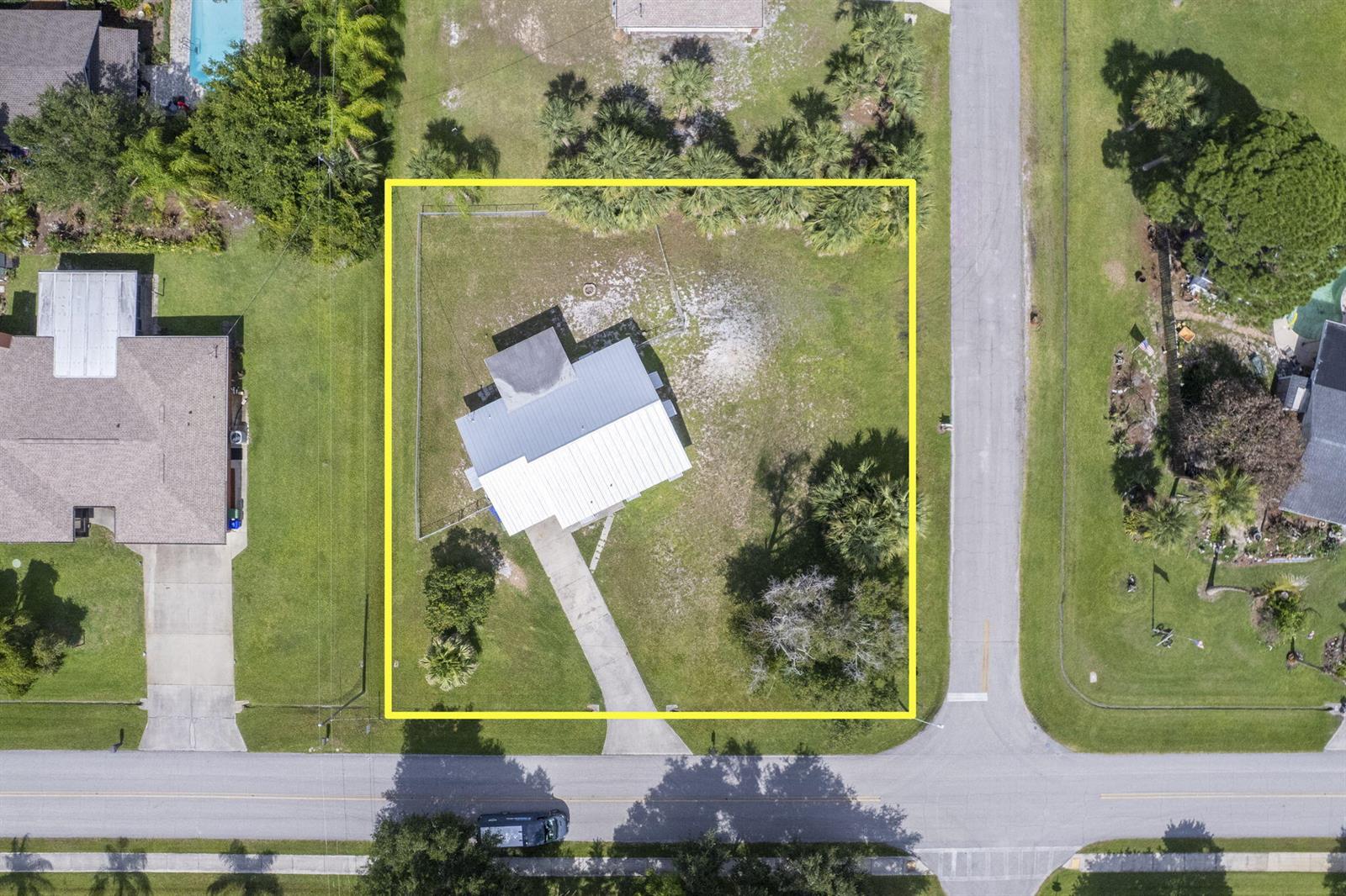 An aerial view shows a house with a metal roof on a fenced corner lot — 273 Easy Street, Sebastian FL 32958, SEBASTIAN, FL