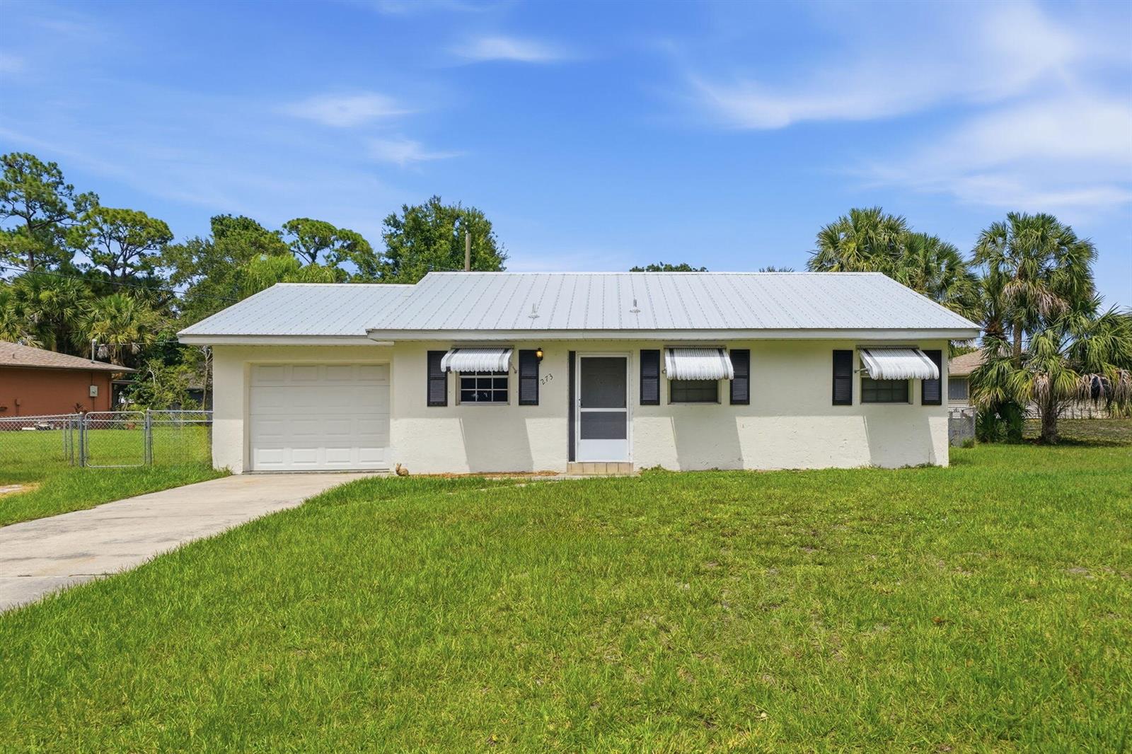 A single-story house with a white stucco exterior, metal roof, and attached garage — 273 Easy Street, Sebastian FL 32958, SEBASTIAN, FL