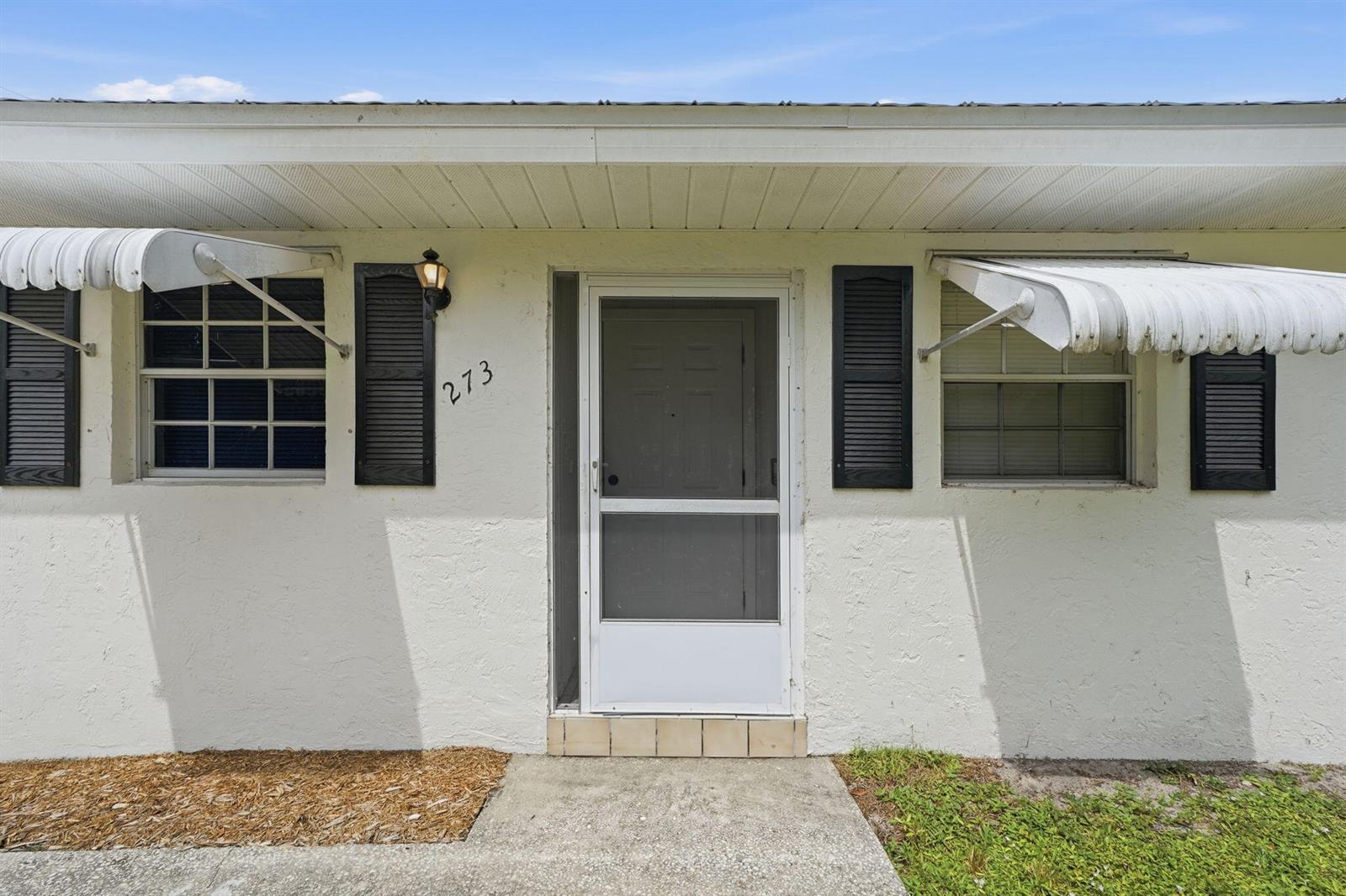 The exterior of a white house features a front door, two windows, and metal awnings — 273 Easy Street, Sebastian FL 32958, SEBASTIAN, FL