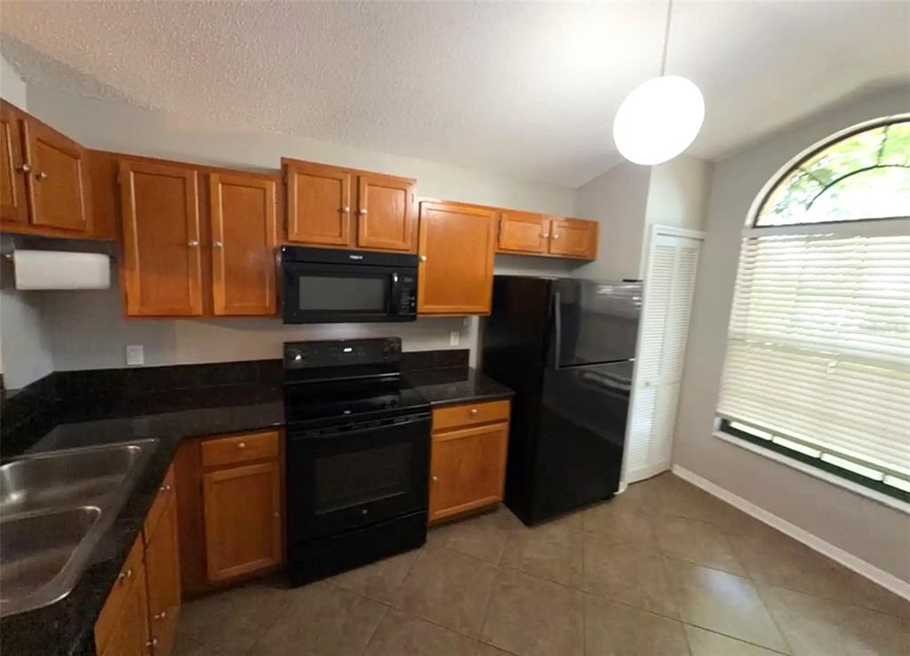 A kitchen with wood cabinets, black appliances, dark countertops, and an arched window — 2201 GRASMERE DRIVE, APOPKA, FL