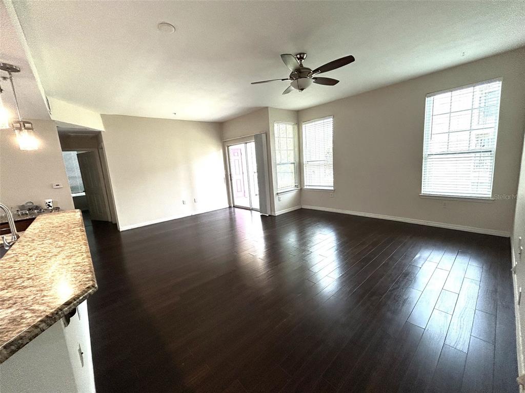 An empty living room features dark wood flooring, a ceiling fan, and large windows — 2015 ERVING CIRCLE UNIT 208, OCOEE, FL