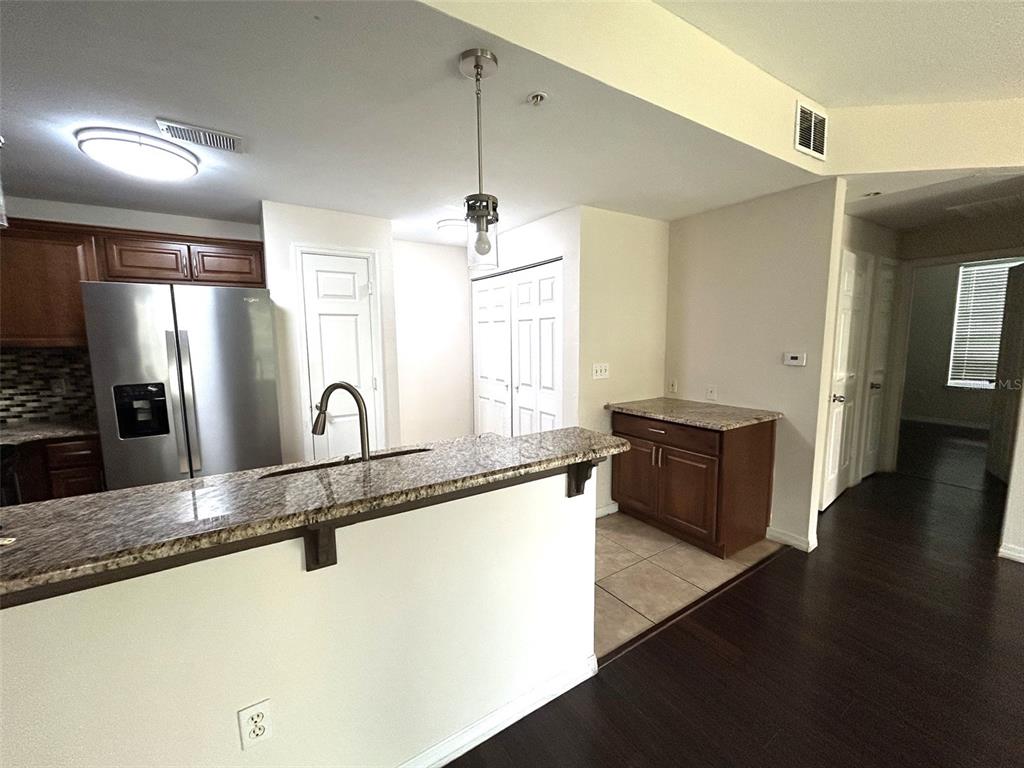A kitchen features a granite breakfast bar, stainless steel refrigerator, and dark wood cabinetry — 2015 ERVING CIRCLE UNIT 208, OCOEE, FL
