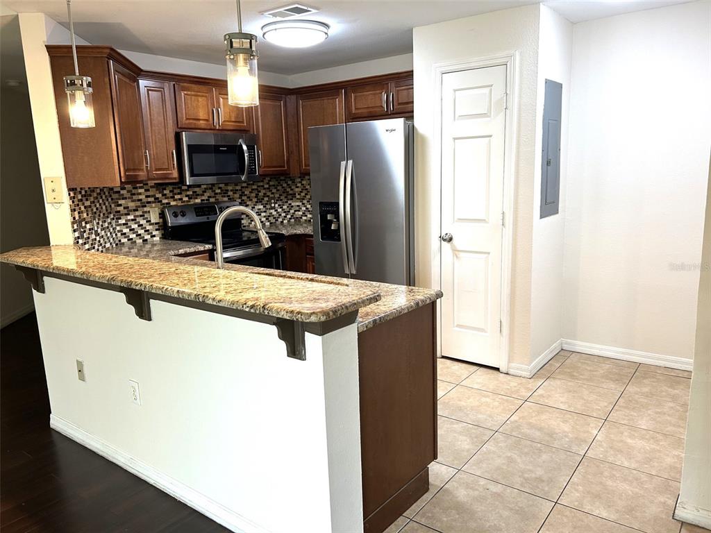 A kitchen features wood cabinets, granite countertops, stainless steel appliances, and a breakfast bar — 2015 ERVING CIRCLE UNIT 208, OCOEE, FL